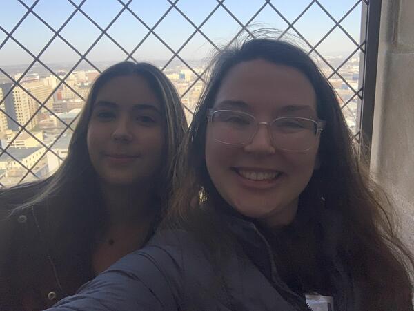 Two women smile for a selfie on a tall building