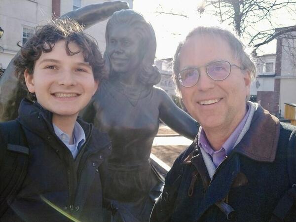 Two men pose for a selfie with a statue behind them