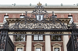 The front gate of Barnard College. A brick building is in the background with a wrought iron fence in the front, which says "Barnard College of Columbia University"