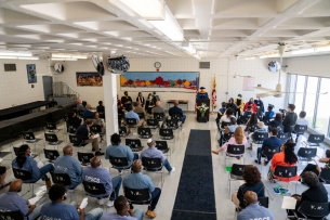 A group of faculty and inmates sit in a large room while Goucher College president Kent Devereaux speaks