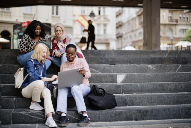 Students sit on the steps near the college and look at the laptop and digital tablet and talk