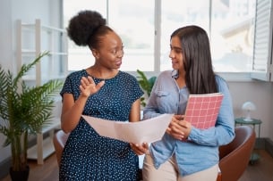 A photo of two women engaging in discussion in an office, suggesting the theme of mentorship and collaboration.