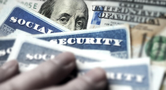 A photo of a stack of Social Security cards atop a $100 bill.