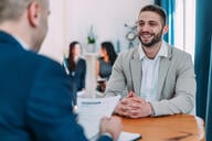 Shot of male HR manager looking through résumé and asking young man questions about his skills and previous job experience.