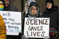 A person in a jacket holds a white sign that says "science saves lives" in black text