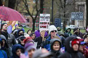 Protesters hold signs imploring Harvard University to resist the demands of President Trump's administration.