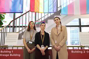 Instructor Ariel Beccia and associate professors Julia Marcus and Brittany Charlton pose in front of a series of LGBTQ flags.