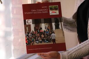 An unidentified person holds a printed version of the University of Louisville Oral Comm Success Guide